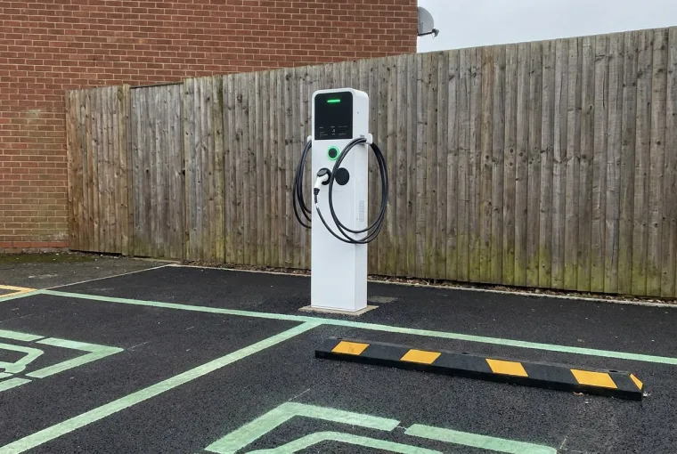 Energised white EV charge point on fresh tarmac with green-marked charging bays on a completed site